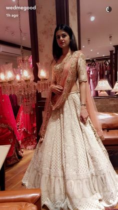 a woman standing in front of a chandelier wearing a white dress with pink and gold accents