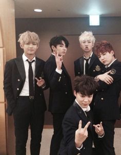 group of young men in black suits posing for the camera with one hand up and two fingers down