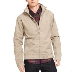 Tan Khaki Jacket With Two Front Pockets, Adjustable Button Cuffs, Two Hidden Pockets On The Inside, Zipper Closure Down The Front And Tommy Emblem On Top Left Casual Cotton Outerwear With Button Cuffs, Casual Khaki Outerwear With Button Cuffs, Casual Winter Outerwear With Button Cuffs, Casual Hooded Outerwear With Button Cuffs, Tommy Hilfiger Classic Winter Outerwear, Classic Tommy Hilfiger Winter Outerwear, Tommy Hilfiger Fall Outerwear With Pockets, Tommy Hilfiger Classic Long Sleeve Outerwear, Classic Tommy Hilfiger Long Sleeve Outerwear