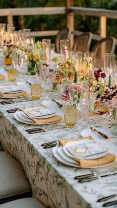 a long table set with place settings and flowers on it for an outdoor dinner party