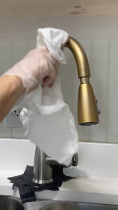 a person in white gloves is cleaning a sink with a gold faucet and tissue