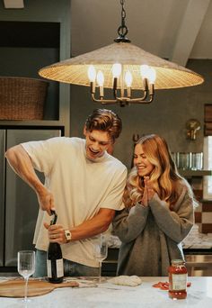 a man standing next to a woman in front of a wine bottle on a counter