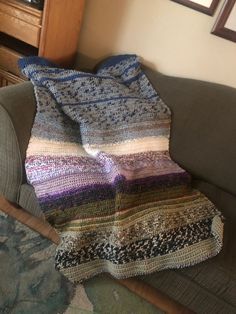 a multicolored crocheted blanket sitting on top of a couch next to a window