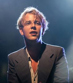 a man with glasses and a suit jacket standing in front of a microphone on stage