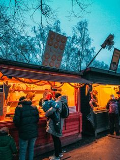 people are standing in line to get food at an outdoor stand with lights on it