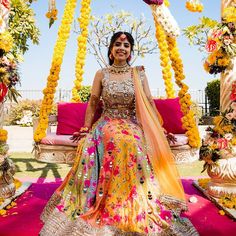 a woman in a yellow and pink dress sitting on a swing with flowers around her