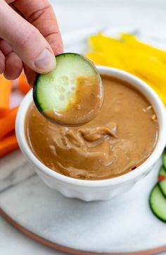 the best thai peanut sauce in a white bowl with cucumbers and carrots