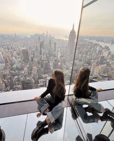 two young women sitting on the edge of a high rise looking out over new york city