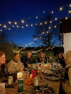 a group of people sitting around a wooden table with food and drinks on it at night