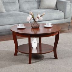 a coffee table with two cups on it in front of a gray couch and rug