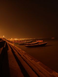 two boats are sitting on the water at night time, with city lights in the background