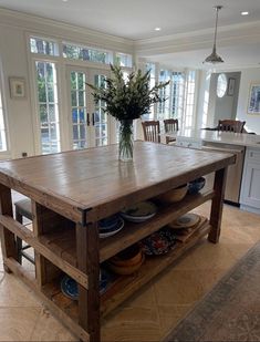 a wooden table with plates and bowls on it in the middle of a large kitchen