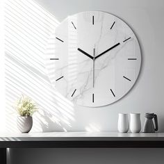 a white clock sitting on top of a table next to a potted plant and two mugs