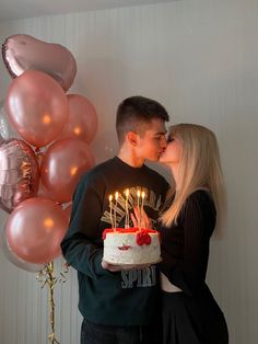 a man and woman kissing in front of a cake with candles on it, surrounded by balloons