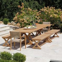 a wooden table sitting on top of a stone floor next to bushes and shrubbery