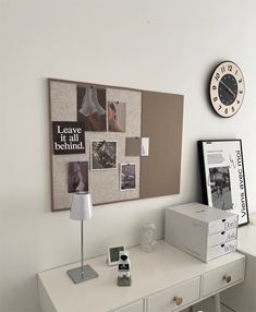 a white desk topped with a lamp next to a clock and pictures on the wall