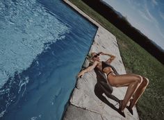 a woman laying on top of a rock next to a pool