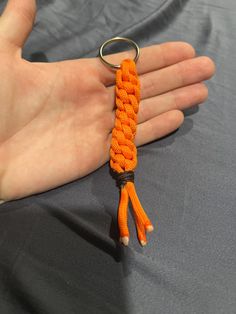 a hand holding an orange rope keychain on top of a gray cloth covered surface