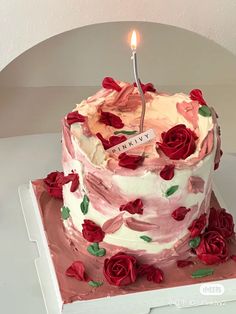 a birthday cake with roses on it and a single candle in the middle that is lit