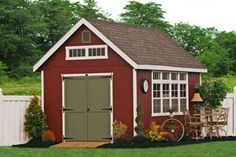 a small red shed sitting on top of a lush green field next to a white fence