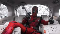 a deadpool is sitting in the back seat of a car and holding a knife