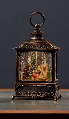 a small metal lantern with christmas trees inside it on a table next to a wall