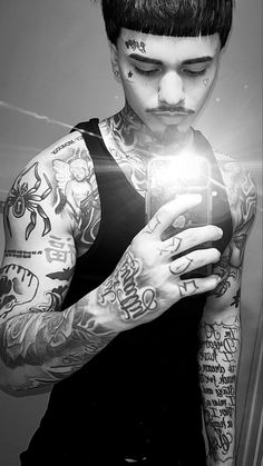 a man with tattoos is looking at his cell phone while standing in front of a mirror