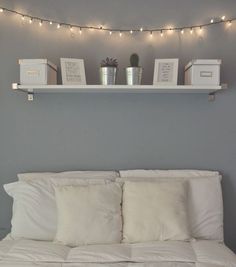 a white bed topped with pillows and blankets under a string of light strung over the headboard