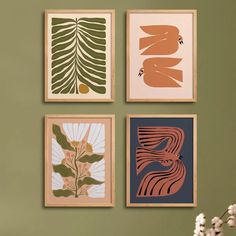 four framed art pieces hang on the wall above a vase with white flowers in it