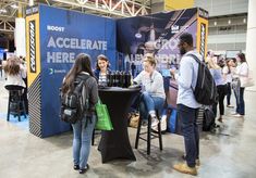 people standing around a table with bottles of wine on it at an exhibit hall or convention