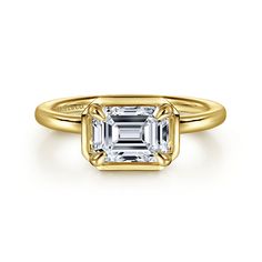 a yellow gold ring with an emerald cut diamond in the center and a roped band around it