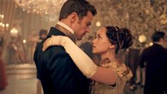 a man and woman dressed in period costumes dance together at a formal event with chandeliers hanging from the ceiling