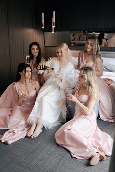 a group of women in pink dresses sitting on the floor drinking wine and having fun