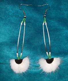 pair of earrings with white feathers and beads on blue velvet background, closeup view