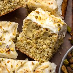 slices of cake with white frosting and pistachios on the side next to nuts