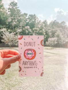 a person holding up a card that says donut anything happens on it in front of some trees