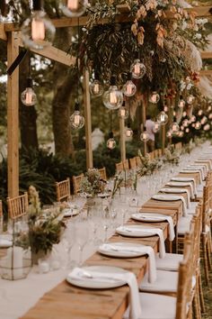 a long table is set up with white linens and greenery hanging from the ceiling