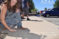 a woman kneeling down on the ground with her hand over her knees while another man stands behind her