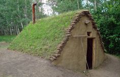 a small house made out of grass with a door in the center and a green roof