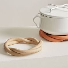 a white pot and two wooden rings sitting on top of a table next to each other