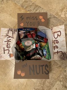 a box filled with nuts and snacks on top of a tile floor next to a sign that says, i miss your