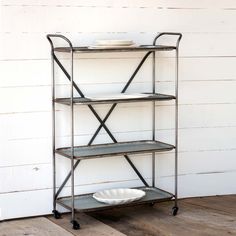 three tiered metal shelf with plates on it against a white painted wall and wood flooring