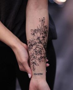 a woman with a flower tattoo on her arm holding onto another person's hand