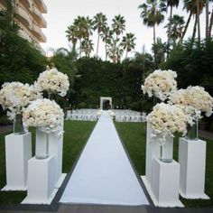 an outdoor ceremony setup with white flowers and tall vases on either side of the aisle