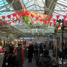 many people are shopping in an open market area with flags hanging from the ceiling above them