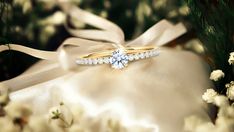 a diamond ring sitting on top of a white satin bag next to flowers and greenery