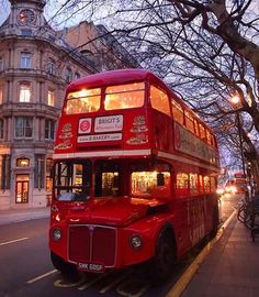 a red double decker bus parked on the side of the road next to a tree