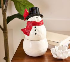 a snowman figurine sitting on top of a table next to a potted plant