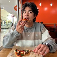 a man sitting at a table with a slice of pizza in front of his mouth