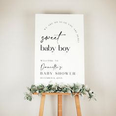 a welcome sign for a baby shower with greenery on the easel and white background